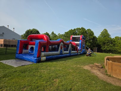 Large red and blue inflatable obstacle course set up on a grassy field at an outdoor event.