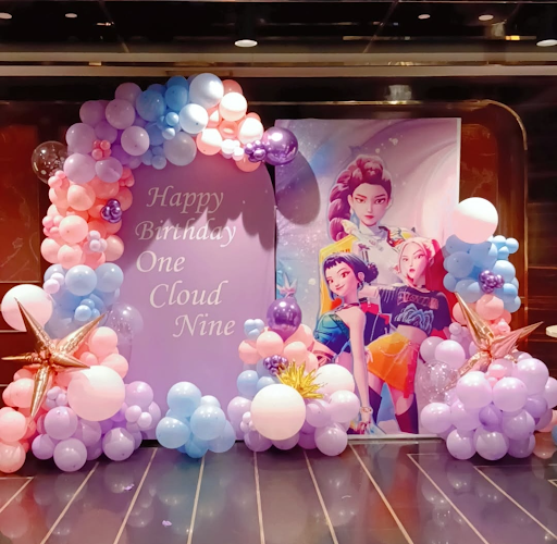The image shows a birthday party decoration setup with a backdrop featuring pastel pink, blue, an… post image