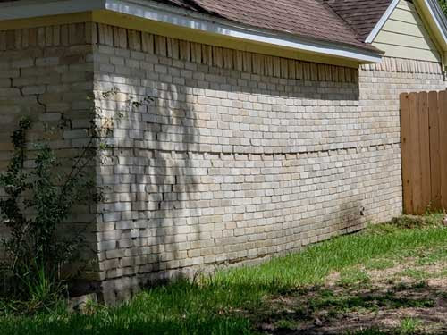 Soil settlement has damaged the slab foundation and created a bow in the brick wall.