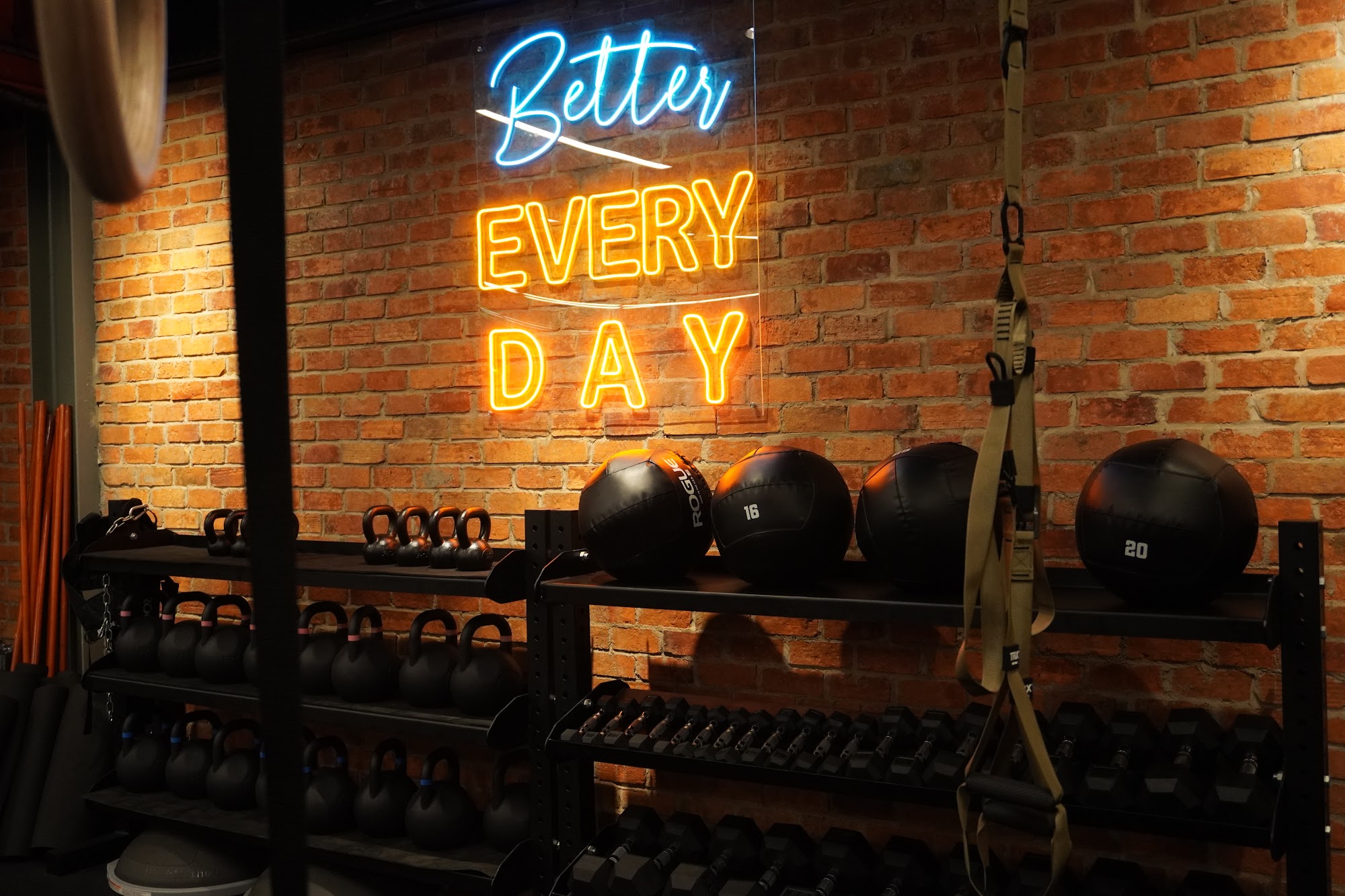 The image shows an interior of a gym or fitness center featuring brick walls and various exercise equipment such as kettlebells, dumbbells, medicine b