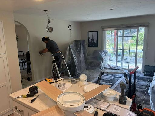 Contractor installing a ceiling fixture in a living room under renovation, surrounded by tools and materials.