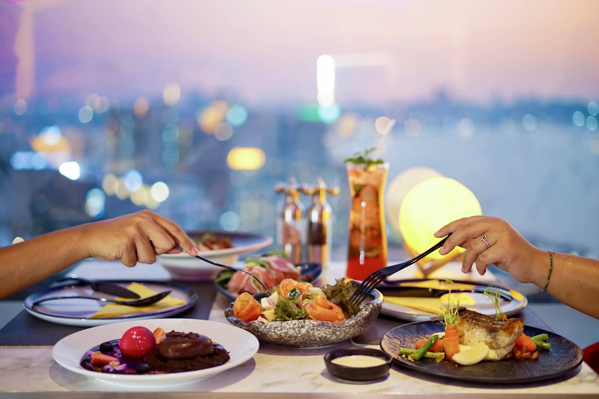 Two people dining at a rooftop restaurant with a city view.