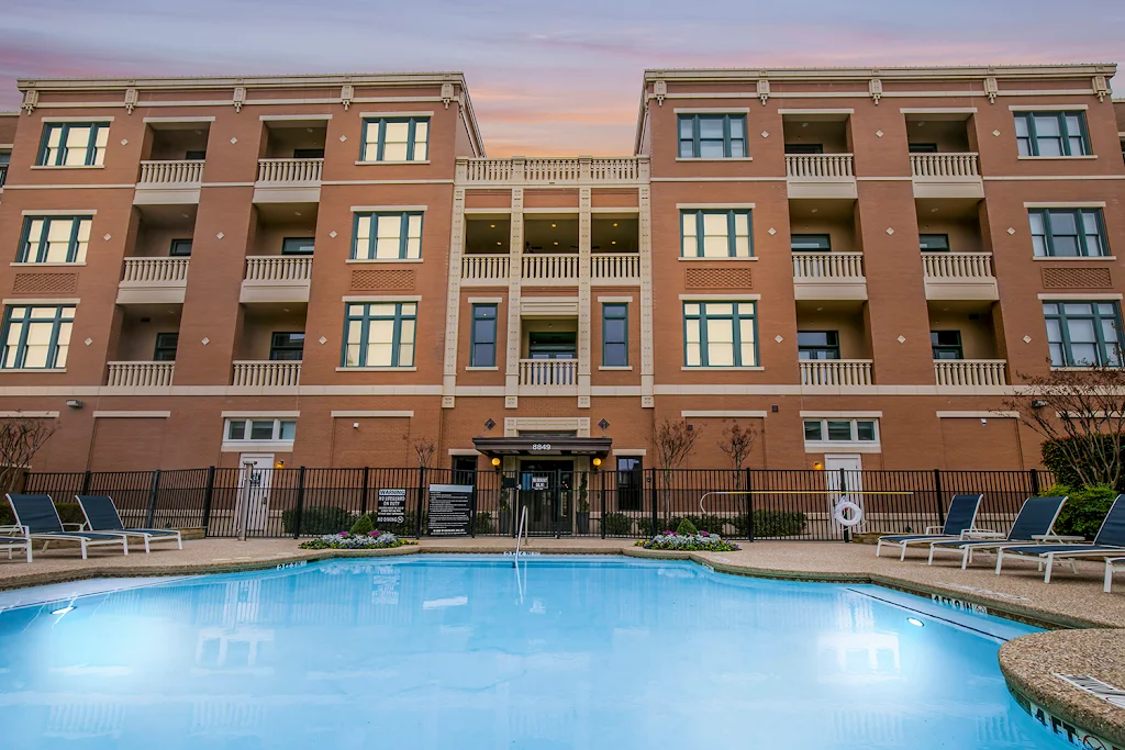 Swimming pool, next to apartment buildings, with several lounge chairs at dusk