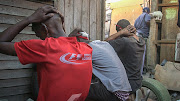 Three men are told to wait with their hands behind their heads while members of the Neighbourhood Safety Team search their homes. 