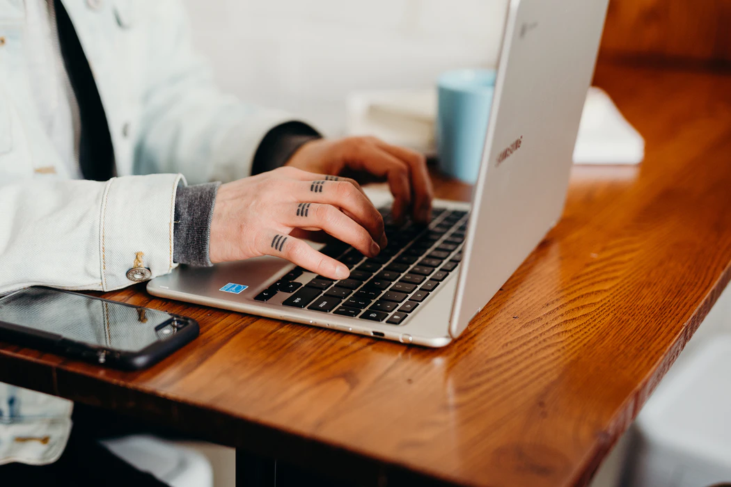 Close up shot of tattooed hands typing on a laptop keyboard.