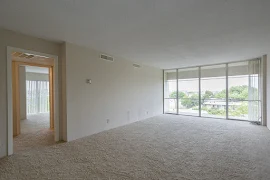 Opposite end of living room facing floor to ceiling window with neutral colored carpet and walls