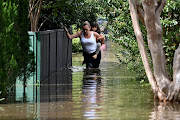 A woman and child walk through floodwater in Windsor, northwest of Sydney, Australia, on March 9 2022. Extreme rainfall and flooding has claimed at least 20 lives and caused tens of thousands of residents to flee their homes.