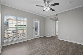 Modern empty apartment room with large windows, a ceiling fan, and hardwood floors, leading to a balcony.