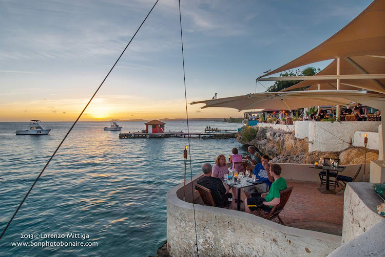 Visitors at a seaside café watch a tropical sunset in Bonaire.