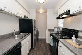 Kitchen with laundry room in back, white cabinets, grey countertops, stainless steel appliances