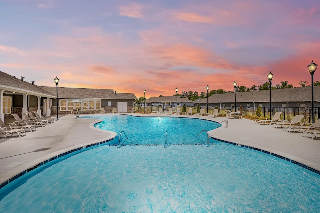 Swimming pool with lounge chairs on the pool deck, outdoor lighting, and view of the clubhouse at dusk 