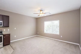 Studio living/bedroom area, facing double window, with ceiling fan, white trim, and gray carpet and walls