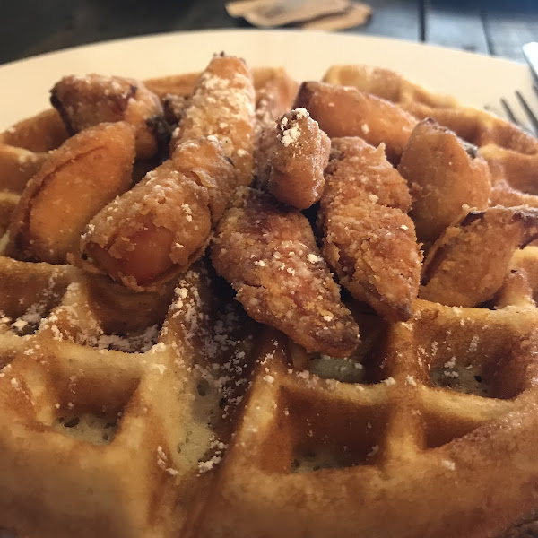 Chicken and waffles served with syrup and hot sauce on the side