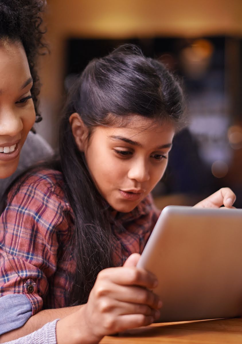 Una donna sorridente e una bambina curiosa guardano insieme lo schermo di un tablet.