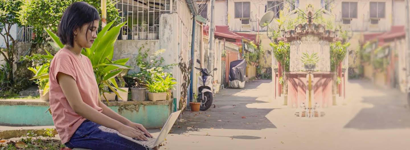 A female student using her Chromebook in a sunny neighborhood alley outdoors.