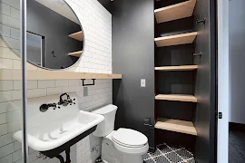 Bathroom with tile inspired floors and walls with dark accent wall with built in wood shelves next to the toilet and sink.