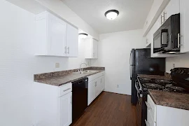 Ktichen with wood-inspired floors, light walls and cabinets, neutral counters & black appliances with dome ceiling lights