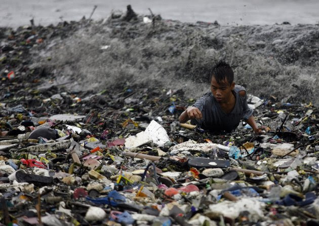 A boy is hit by waves at the height of Typhoon Nanmadol as he collects recyclable materials from garbage washed onto the shore along Manila Bay in Manila