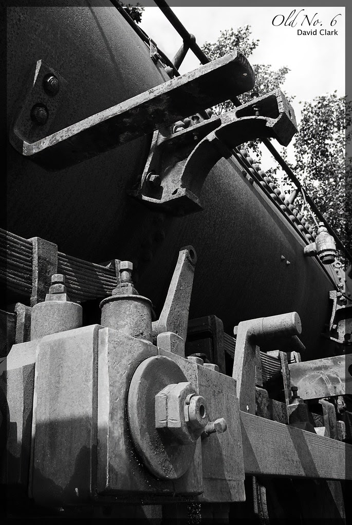 An old steam engine, with many rusted parts, viewed at a sharp angle from the side.