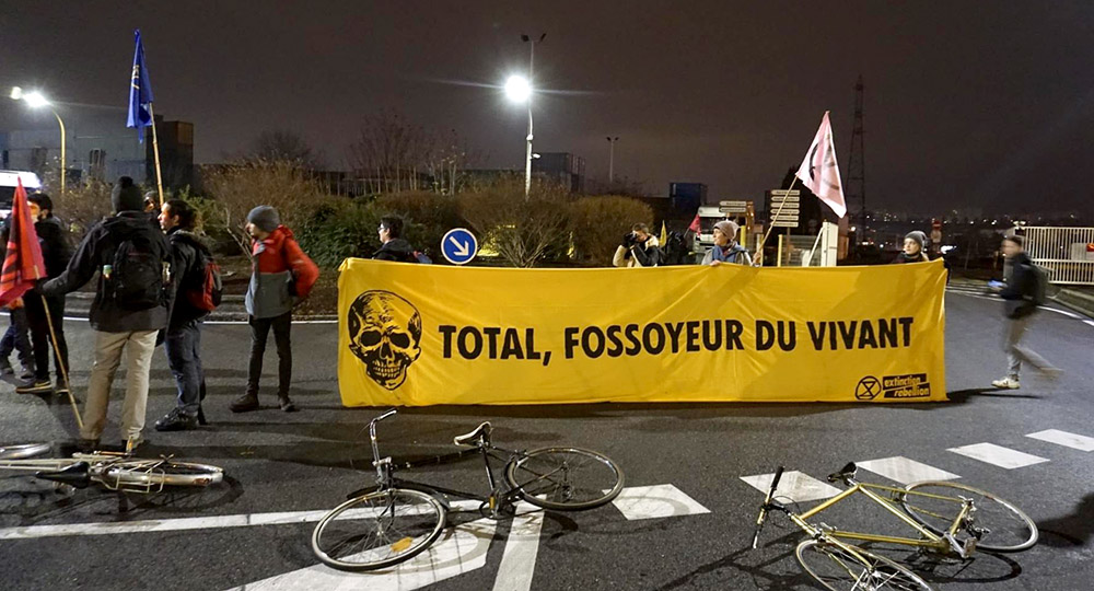 Rebels hold their yellow banner across a drive, bikes left on the tarmac nearby.