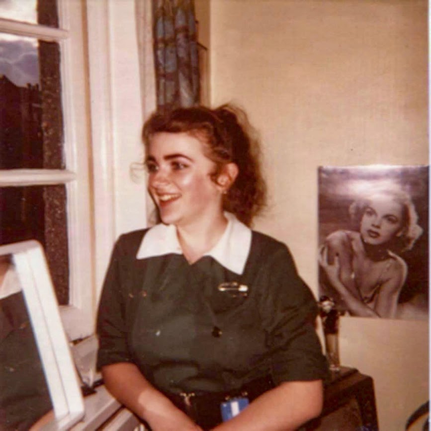 An old photograph of a happy veterinary nurse in front of a Judy Garland poster