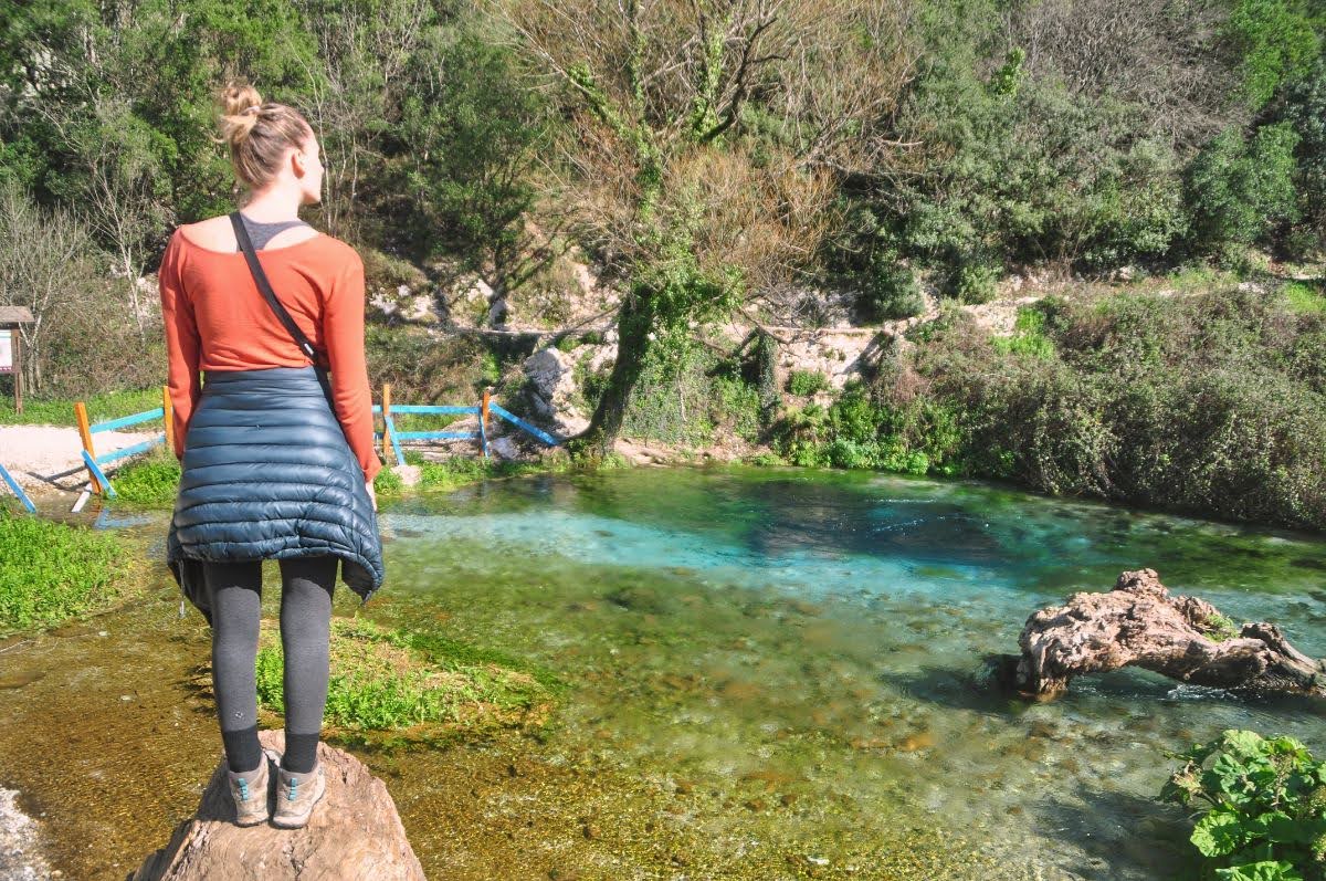 A girl standing on a large log looking at the water at blue eye, vlora county, albania