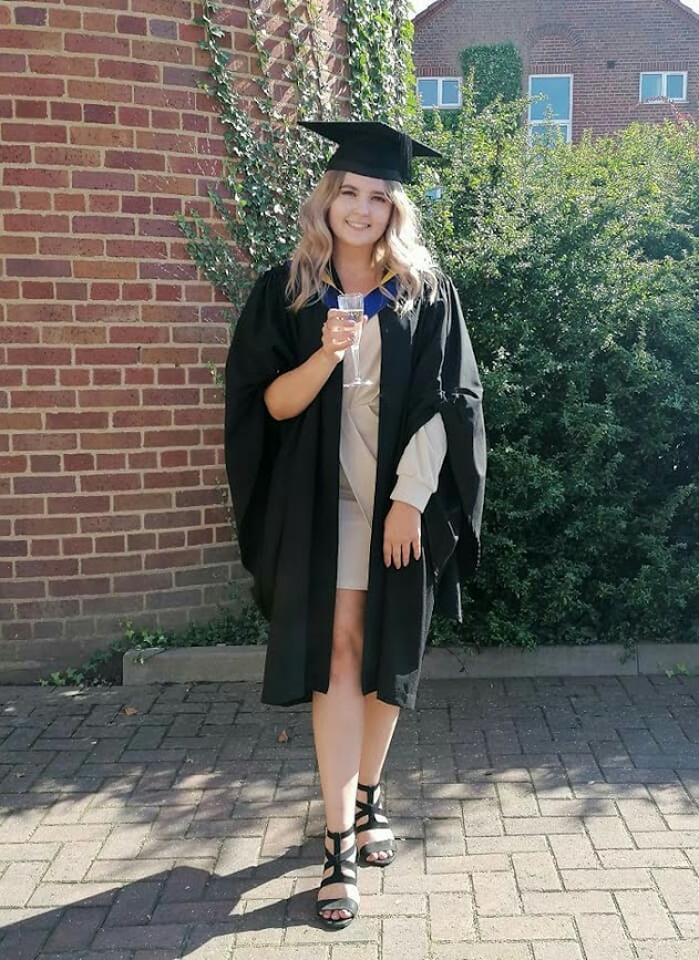 A girl holding a glass of fizzy wearing a graduation cap and gown on her graduation day becoming a qualified veterinary nurse