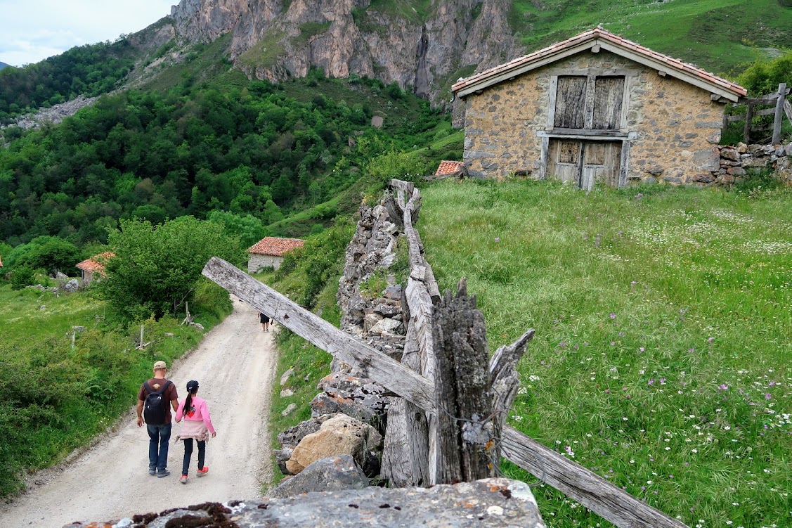 Hikers pass a stone house in a mountain village in the Picos de Europa