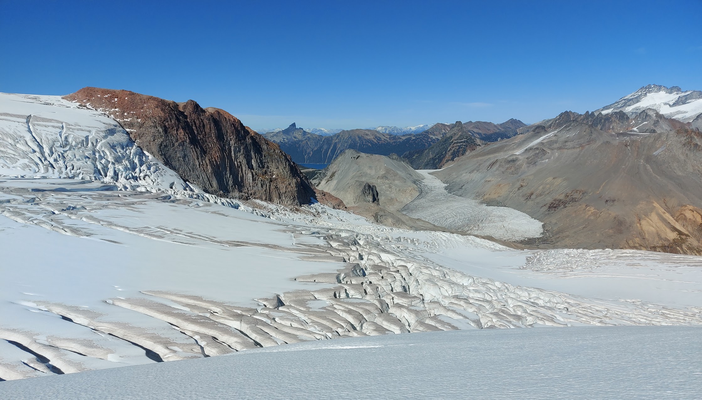 heavily-crevassed terrain, with more mellow glacier and Garibaldi Lake in the background