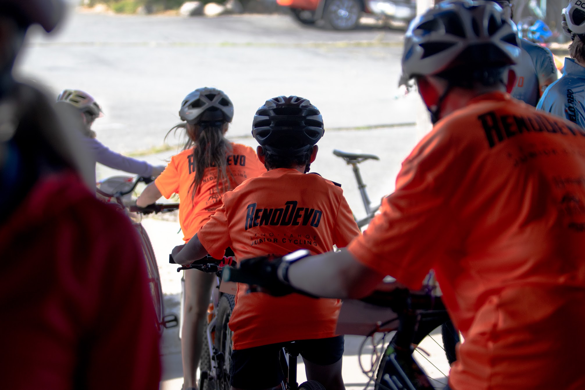 A group of young athletes starting their rides in their bright orange Reno Devo t-shirts.