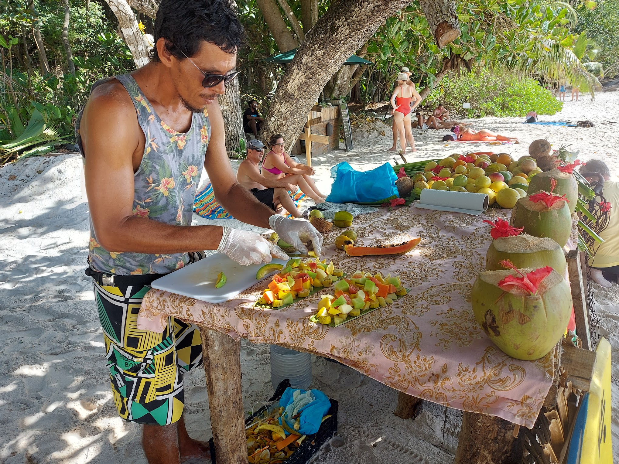 Fruit seller at Anse Georgette preparing a fruit platter, served on a leaf, and red coconuts to drink