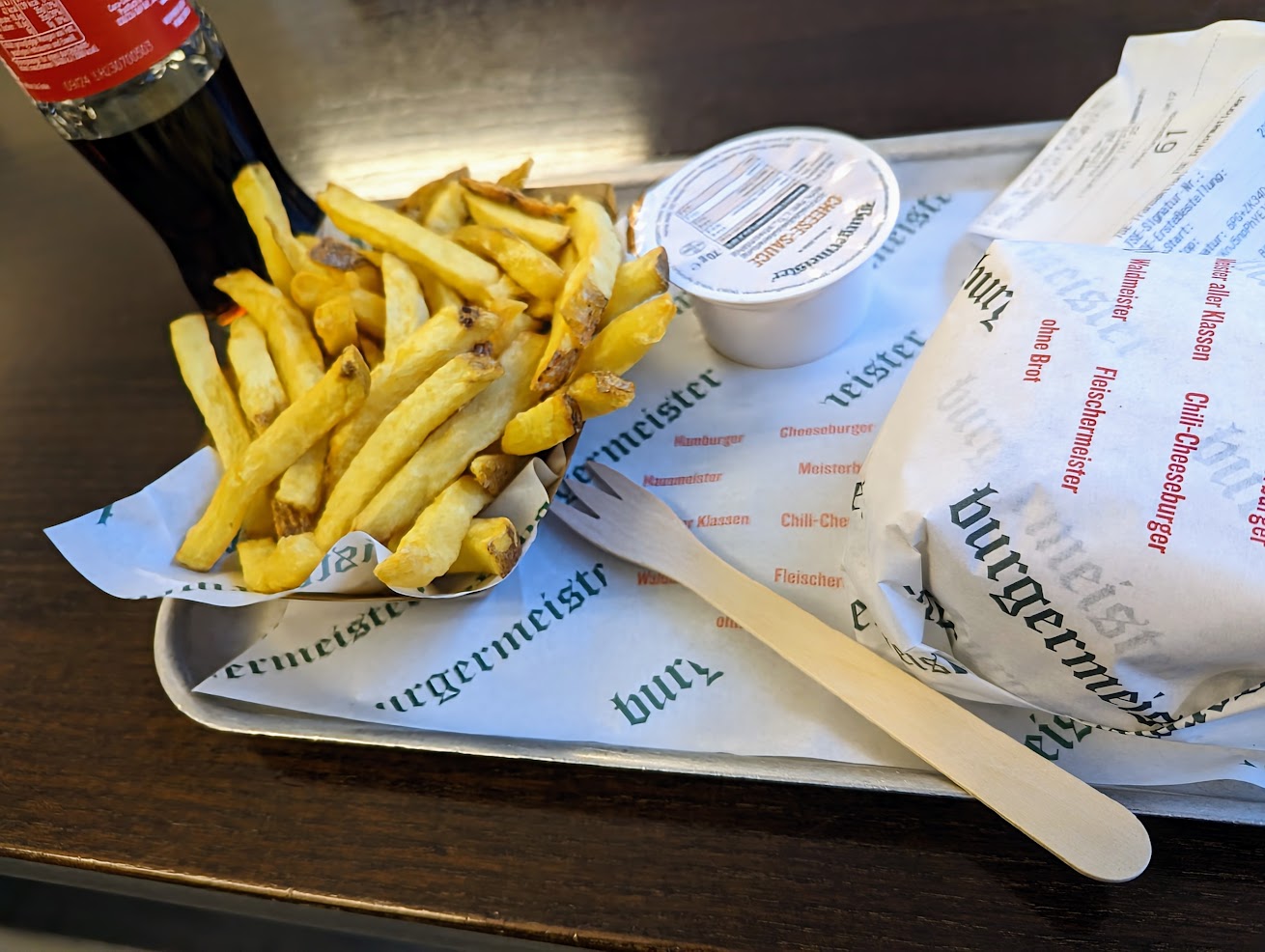 Burger on metal tray with chips and a pot of cheese sauce with a half drunk bottle of coke