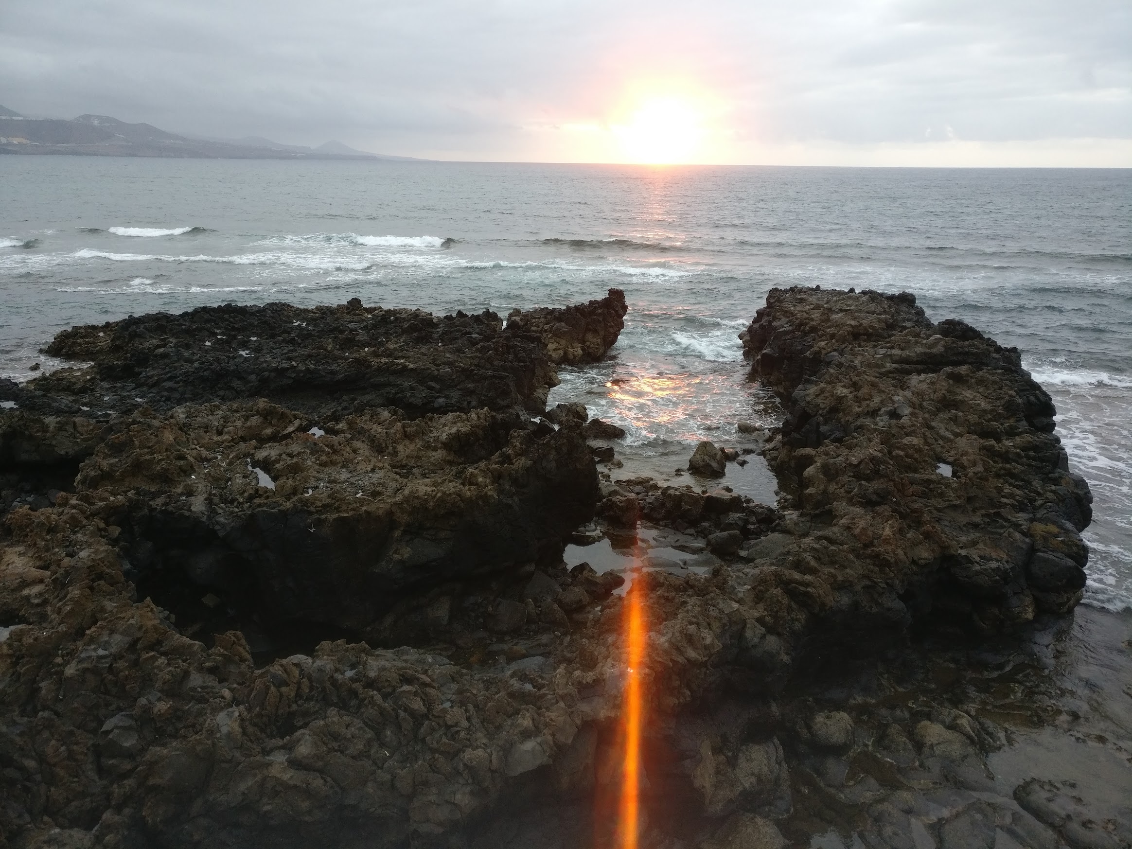 Sunset. A ray of light passes through two symmetric large rocks in the ocean