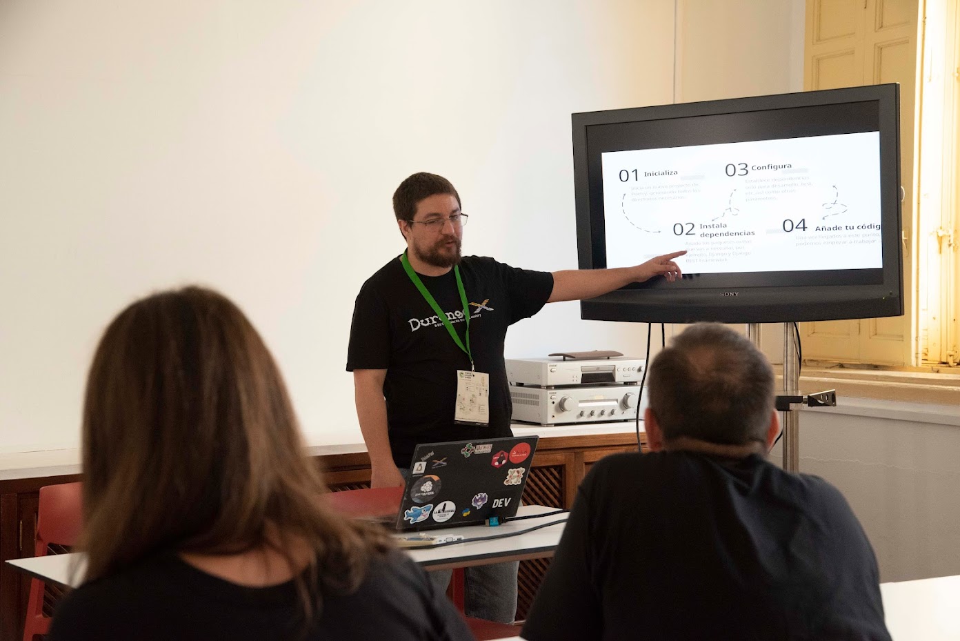 Juanjo llevando una camiseta de DurangoX y exponiendo en un monitor, señalando una diapositiva