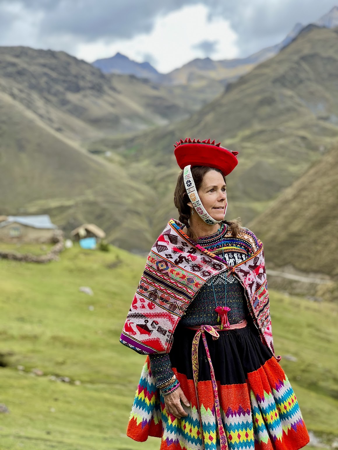 Image is of a woman in colorful clothing standing atop a mountain