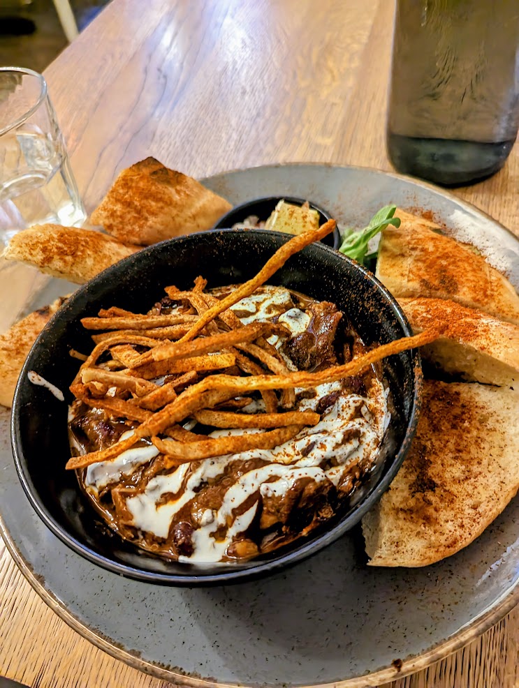 Beef stew with bread and a little sauce around it served in a black bowl