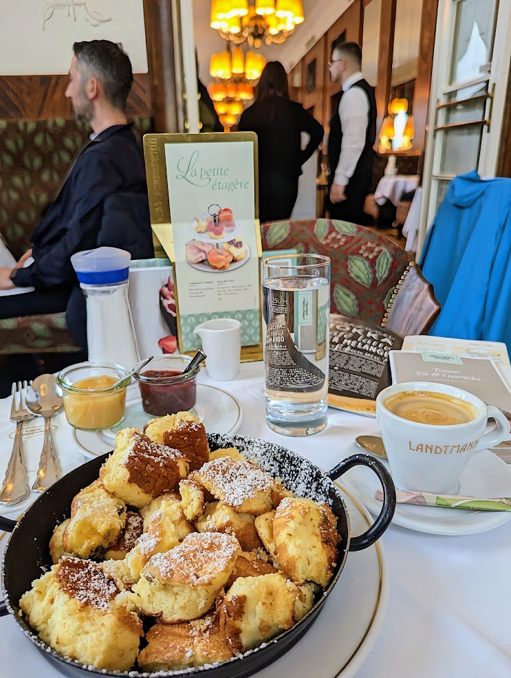 large pancake dish in a hot black iron skillet with coffee and water on a table. Crowded restaurant surroundings