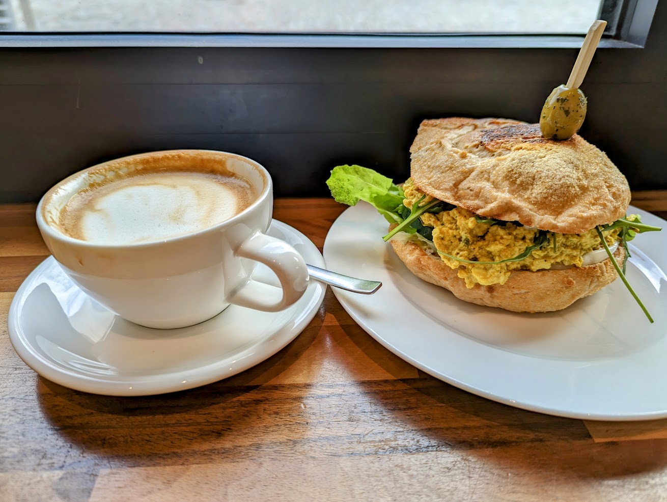 Scrambled tofu sandwich on plate next to a coffee