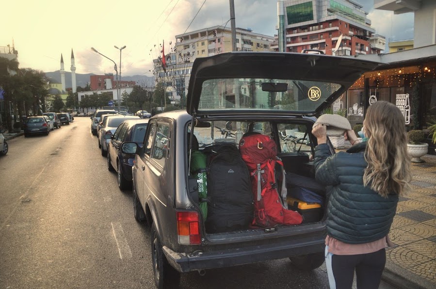 An opened car boot of a 4x4 lada niva car parked in Shkoder City, Albania. A girl stands before the car putting a hat on.