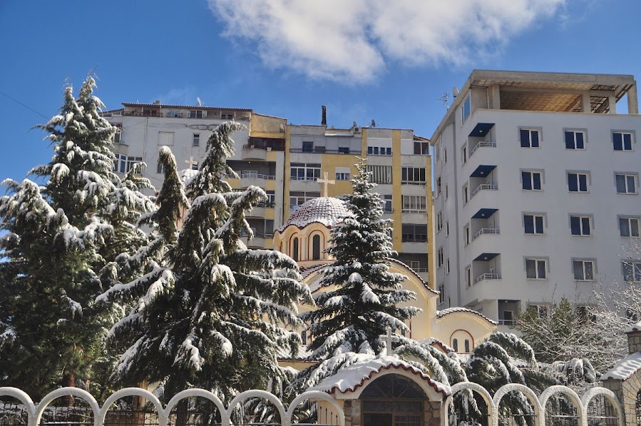 Tall green tress and a church in the snow in the centre of Pogradec, Korce County, Albania in the winter.