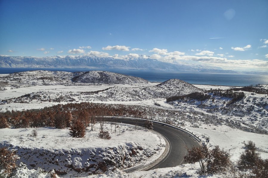 Snow covered road before Lake Ochrid, Korce County, Albania in the winter. Snowy mountains in the distance