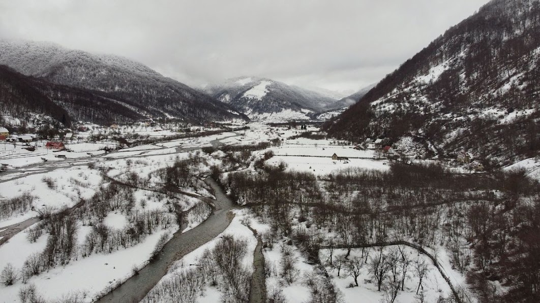 A drone picture of snow covered fields and mountains in Vermosh Valley, Shkoder County, Albania. A meandering river.