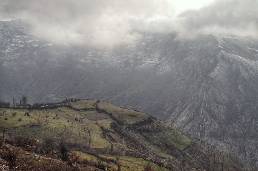 An aerial view of greenfields with snowy mountains in the background in Radomire, Diber County, Albania