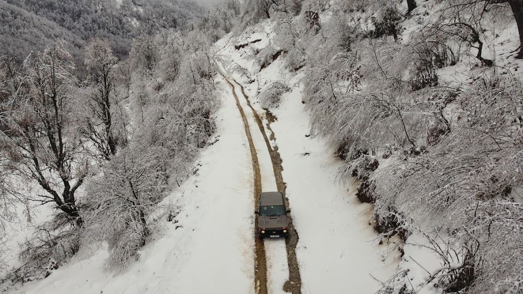 A drone picture of a car driving along a very snowy dirt road in Dragobi village, Valbona Valley, Kukes County, Albania