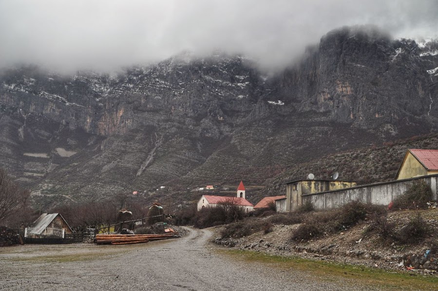 Snowy, rocky mountains in the distance of Nikc, Shkoder County, Albania. A church and houses can be seen.