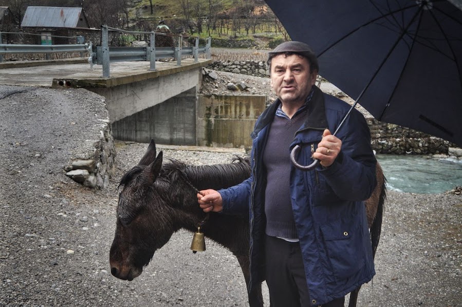 Albanian man holding a donkey with a bell in vukel village, albanian alps