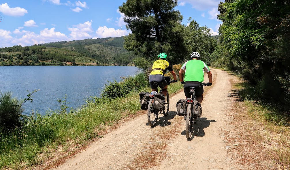 Two men riding bicycles on a gravel road beside a lake in Portugal