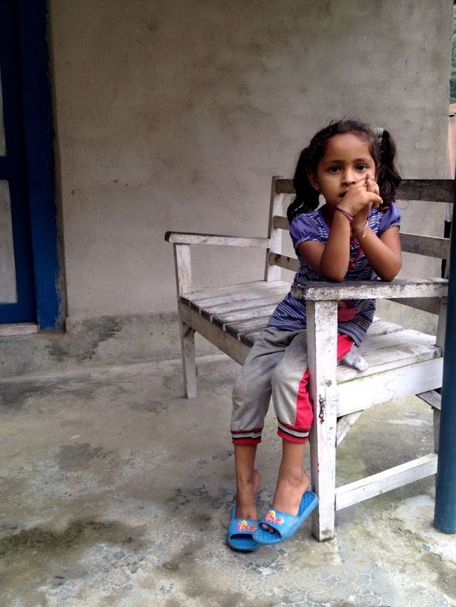 little nepali girl sitting on bench in village in annapurna 