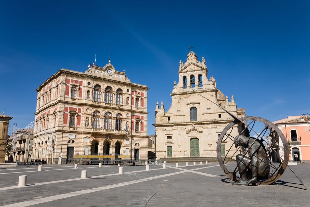 A praça principal da cidade siciliana de Grammichele com prefeitura, igreja matriz e relógio de sol.