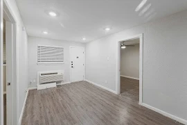 Living room with window with blinds, wood plank flooring, AC unit, light gray walls, and white trim and doors